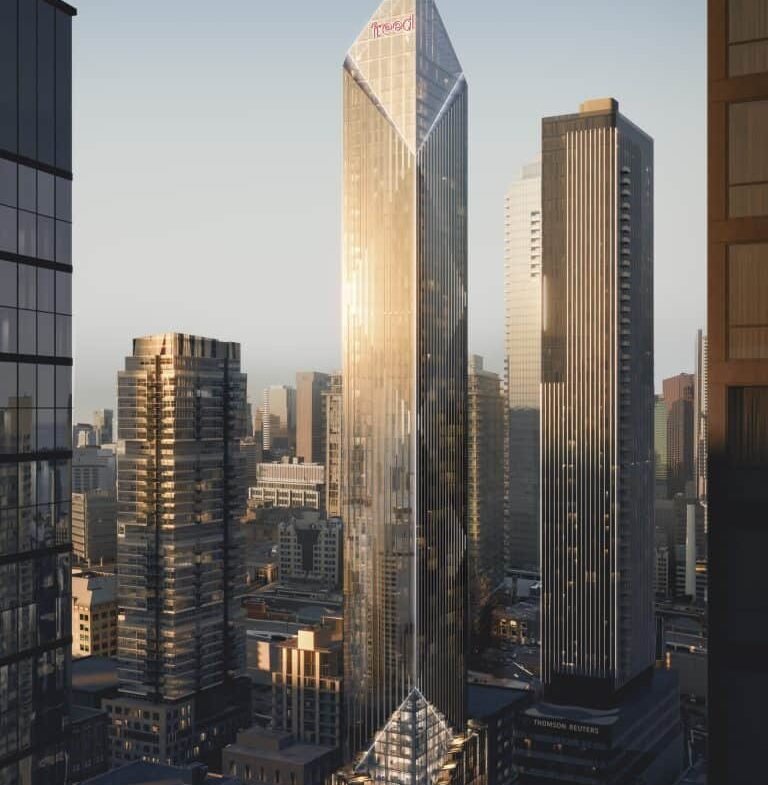 A cityscape at sunrise featuring a skyline of modern skyscrapers. The central building, known as Freed Hotel, is a tall, sleek, glass-encased structure with a pointed top, reflecting golden sunlight. Other buildings of varying heights surround it, including the elegant Freed Residences, with the sky displaying a soft, warm light.