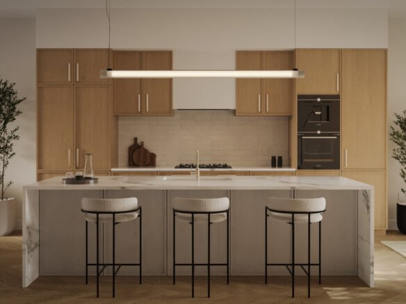 The modern kitchen in new homes in GTA features light wood cabinets, a marble island with three cushioned bar stools, a sleek hanging light fixture, two potted plants, and built-in stainless steel appliances. The room is warmly lit and elegantly organized.