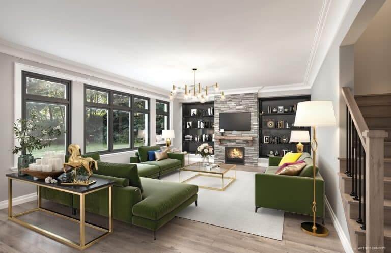 A modern living room in a pre-construction home features a large green sectional sofa, gold-accented furniture, and a stone fireplace. Built-in shelves with decor items surround the fireplace. Expansive windows let in natural light, while a chandelier and floor lamp illuminate the space.
