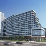 A modern urban intersection showcases a multi-story building with sleek glass and white facades. The scene, reminiscent of new condos' rising skyline, includes several cars on the street and a clear blue sky. People stroll past the building, where trees line the sidewalks gracefully.