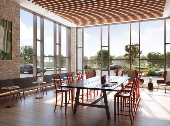 A modern conference room in a new GTA home features a large rectangular table surrounded by red chairs. Sunlight streams through expansive windows, illuminating the space. A bench with a laptop sits on the left, while framed art adorns the textured wall and greenery flourishes outside.