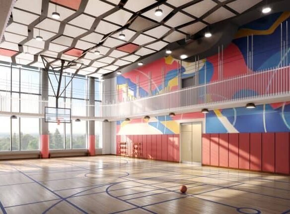A modern indoor basketball court in Sg Homes features a wooden floor and a colorful geometric mural on the walls. Sunlight streams through large windows, highlighting the red padded walls. A basketball rests on the court as ceiling lights illuminate this perfect addition to new homes in GTA.