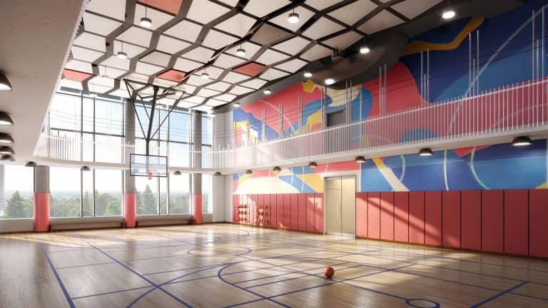 A modern indoor basketball court in Sg Homes features a wooden floor and a colorful geometric mural on the walls. Sunlight streams through large windows, highlighting the red padded walls. A basketball rests on the court as ceiling lights illuminate this perfect addition to new homes in GTA.