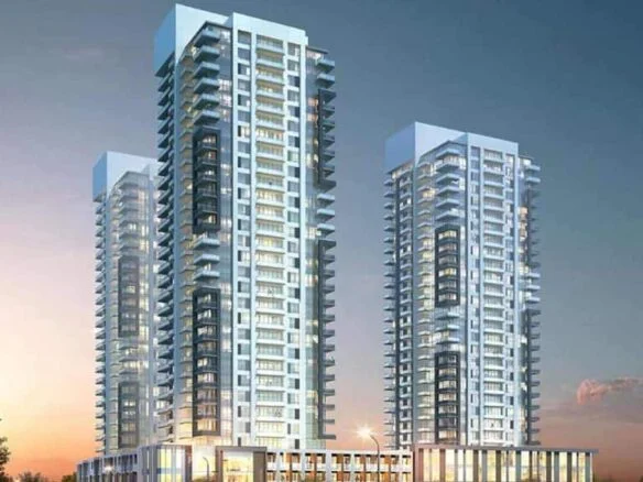 Thompson Towers is a modern complex featuring three tall, glass-clad residential towers with balconies, set against a Sienna sunset sky. The buildings have lower commercial podiums and are surrounded by greenery and a few vehicles on the adjacent road.