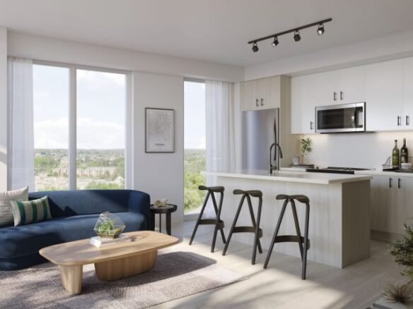 A modern living room and kitchen area in new homes features large windows, a navy sofa, a wooden coffee table, and three bar stools at a kitchen island. The kitchen boasts white cabinets, stainless steel appliances, and track lighting overhead—ideal for contemporary living in the GTA.