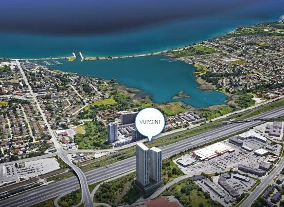 Aerial view of a coastal cityscape reveals "VIP POINT," a tall building near the highway. The mix of residential and commercial areas hints at new homes in GTA, with pre-construction homes promising a vibrant future against the backdrop of a vast shimmering body of water.