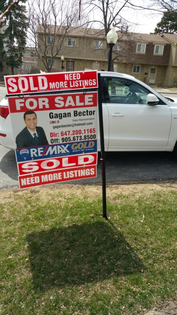 A white car in front of a sold real estate sign.