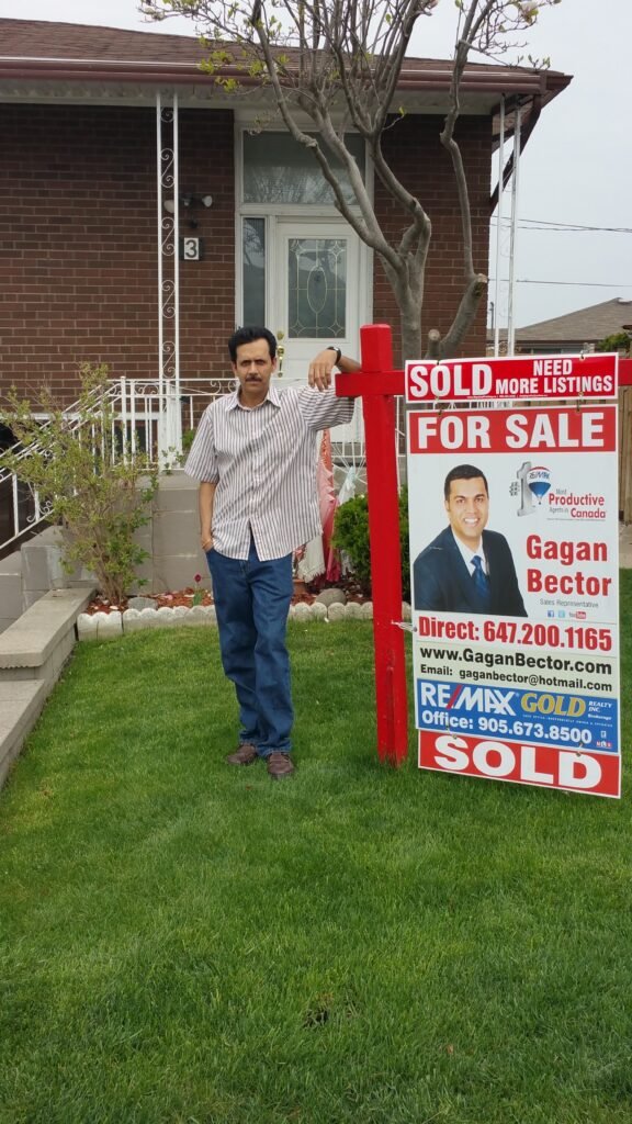A man standing in front of a house with a sold for sale sign.