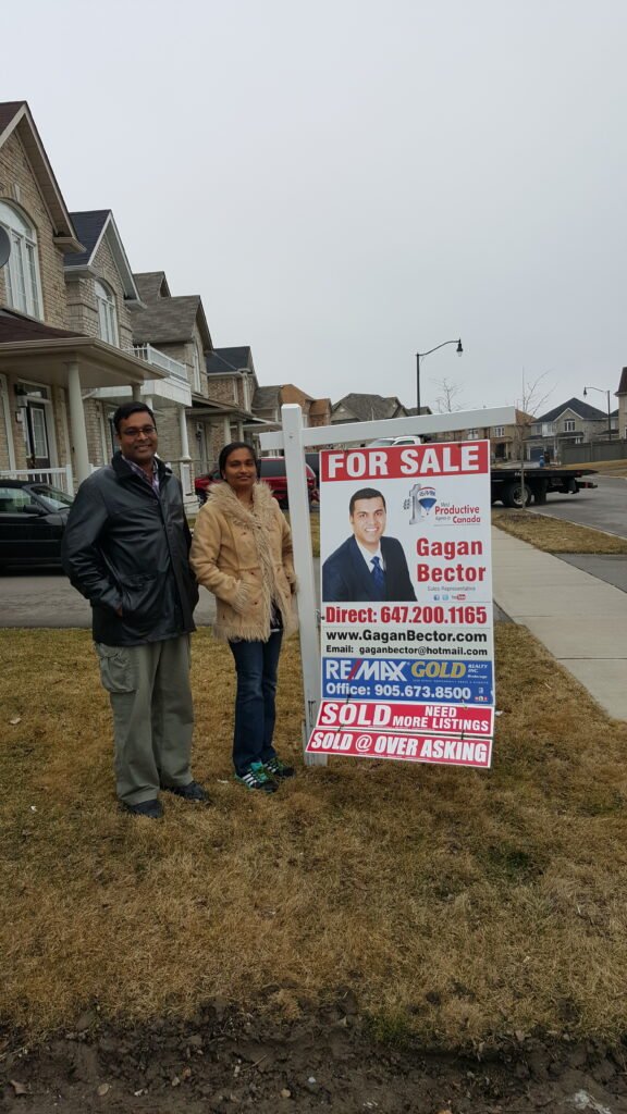 Two people standing in front of a for sale sign.