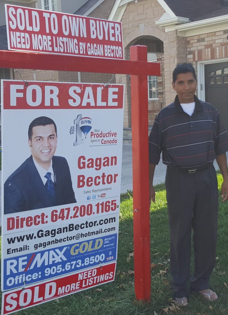 A man standing next to a for sale sign in front of a house.