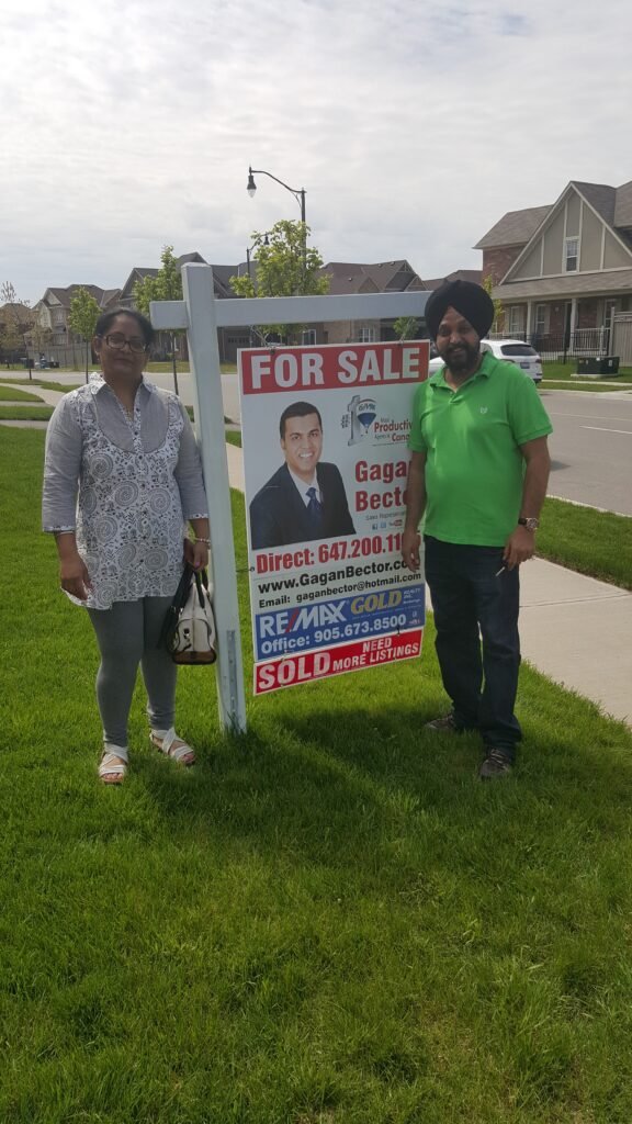 Two people standing in front of a for sale sign.