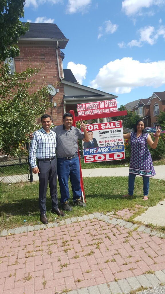 Three people standing in front of a house with a real estate sign.