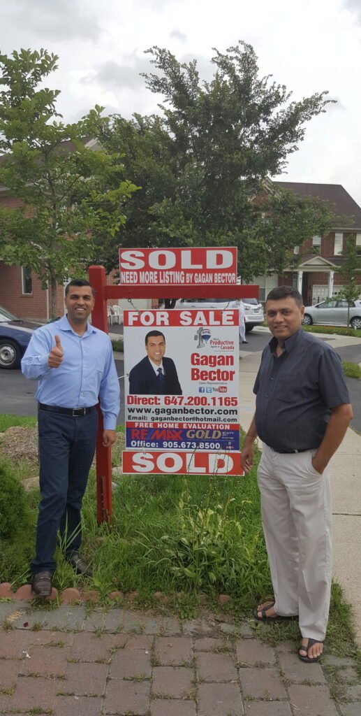 Two men standing in front of a sold sign.