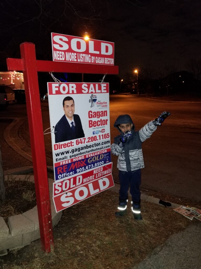 A boy standing in front of a for sale sign.