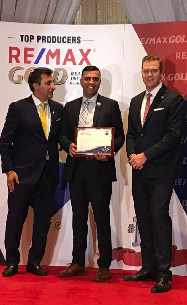 Three men standing in front of a stage with a remax award.
