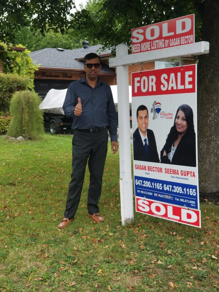 A man standing in front of a sold for sale sign.