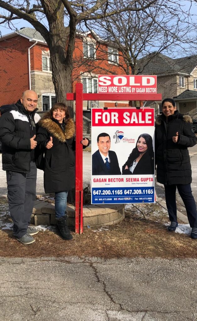 Three people standing in front of a sold for sale sign.