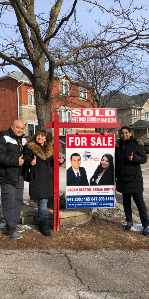 Three people standing in front of a sold for sale sign.