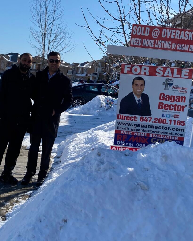 Two men standing in front of a snowy street with a for sale sign.