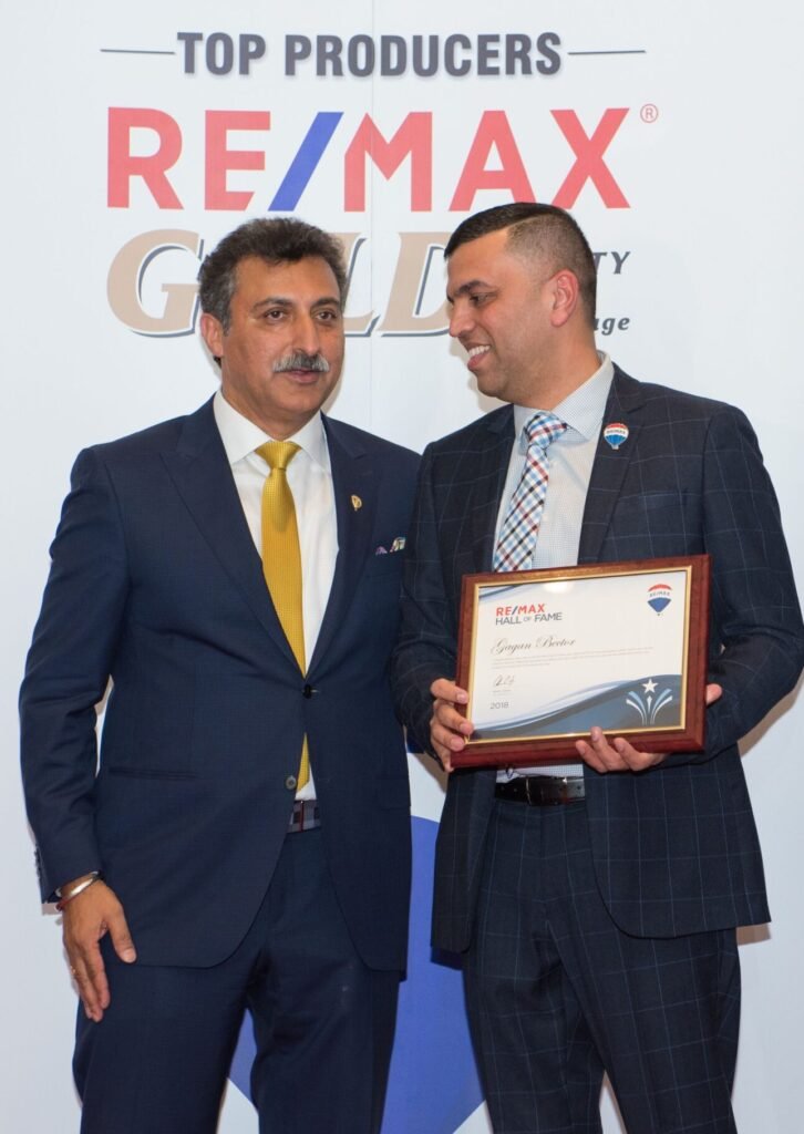 Three men in suits standing next to a sign that says remax gold.