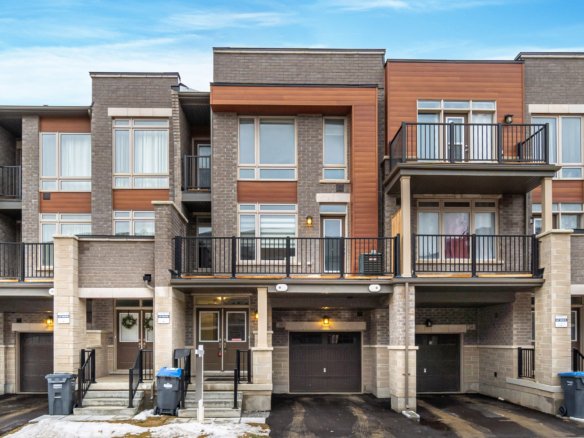A row of modern, multi-story townhouses with brick and wood paneling facades awaits those navigating their transition. Each townhouse has a balcony, garage, and driveway. A light layer of snow is visible on the ground under a clear blue sky—a perfect setting whether you're looking to buy or sell your home first.