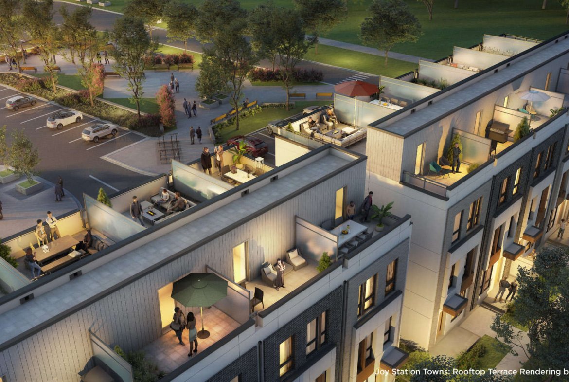 A rooftop terrace rendering of Joy Station Towns depicts modern townhouses with outdoor seating areas, tables, greenery, and people socializing. In the background, a parking area and trees create a lush environment. The scene is set during dusk, with warm lighting enhancing the inviting atmosphere.