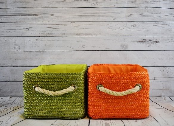 Two woven baskets with rope handles are placed side by side on a wooden floor. The left basket is green, and the right is orange, both set against a white wooden plank background. Such vibrant storage solutions can aid in avoiding downsizing mistakes while maintaining style.